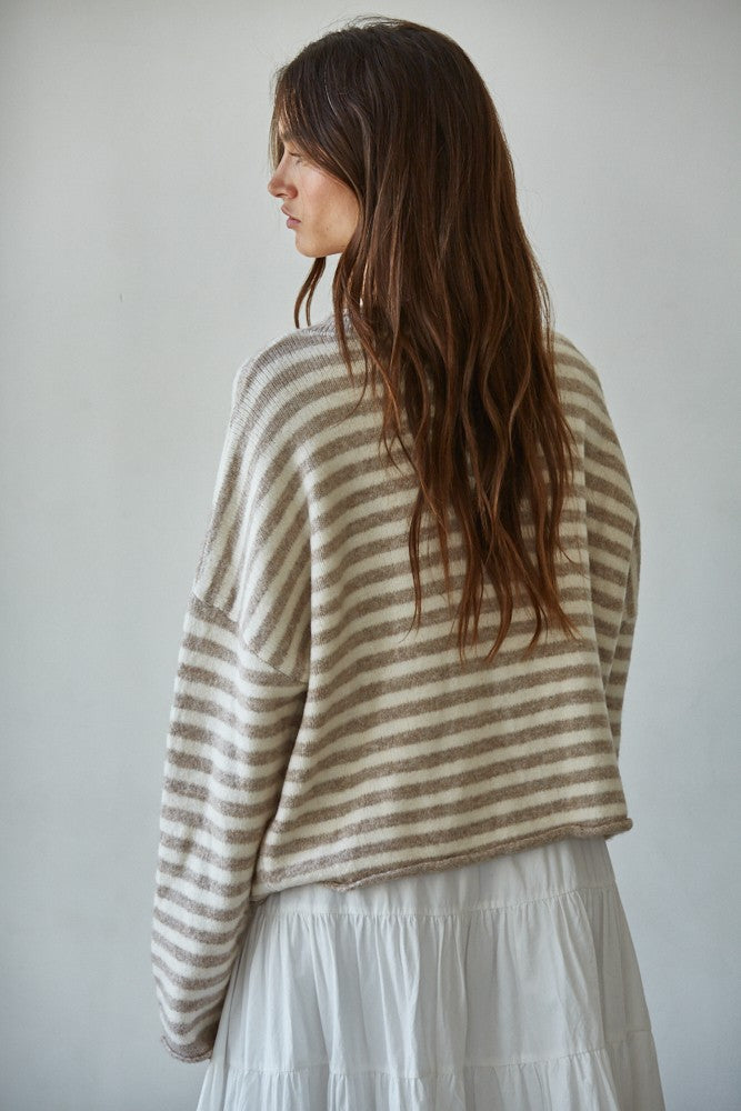 Woman wearing a striped sweater and white skirt against a plain background