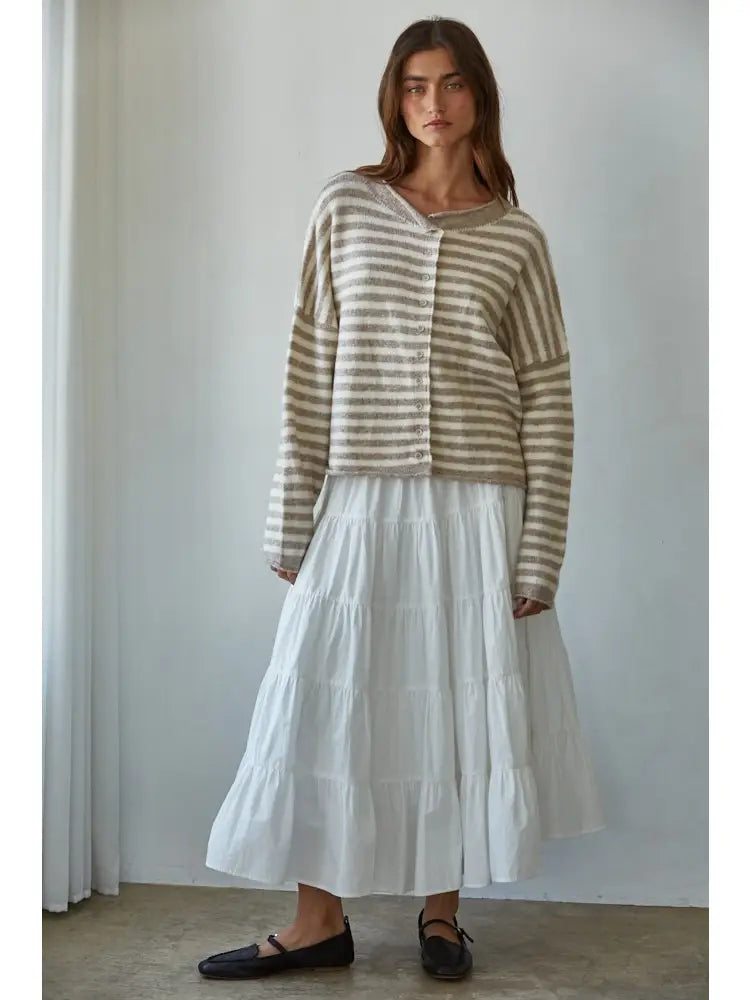 Woman wearing a striped sweater and white skirt against a plain background