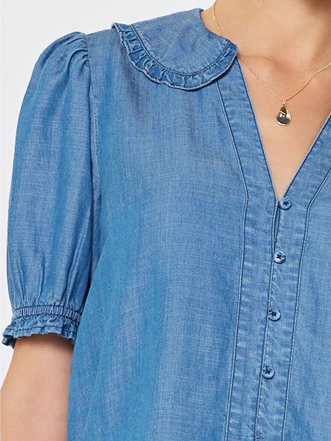 Blue denim dress with ruffled collar and puff sleeves on a plain background