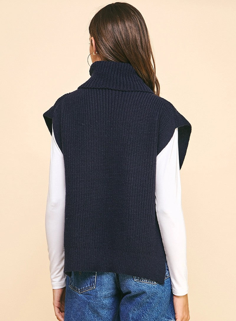 Person wearing a navy blue knitted vest on a beige background