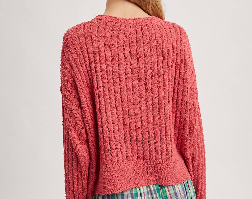 Person wearing a pink chunky knit sweater and plaid skirt on a plain background