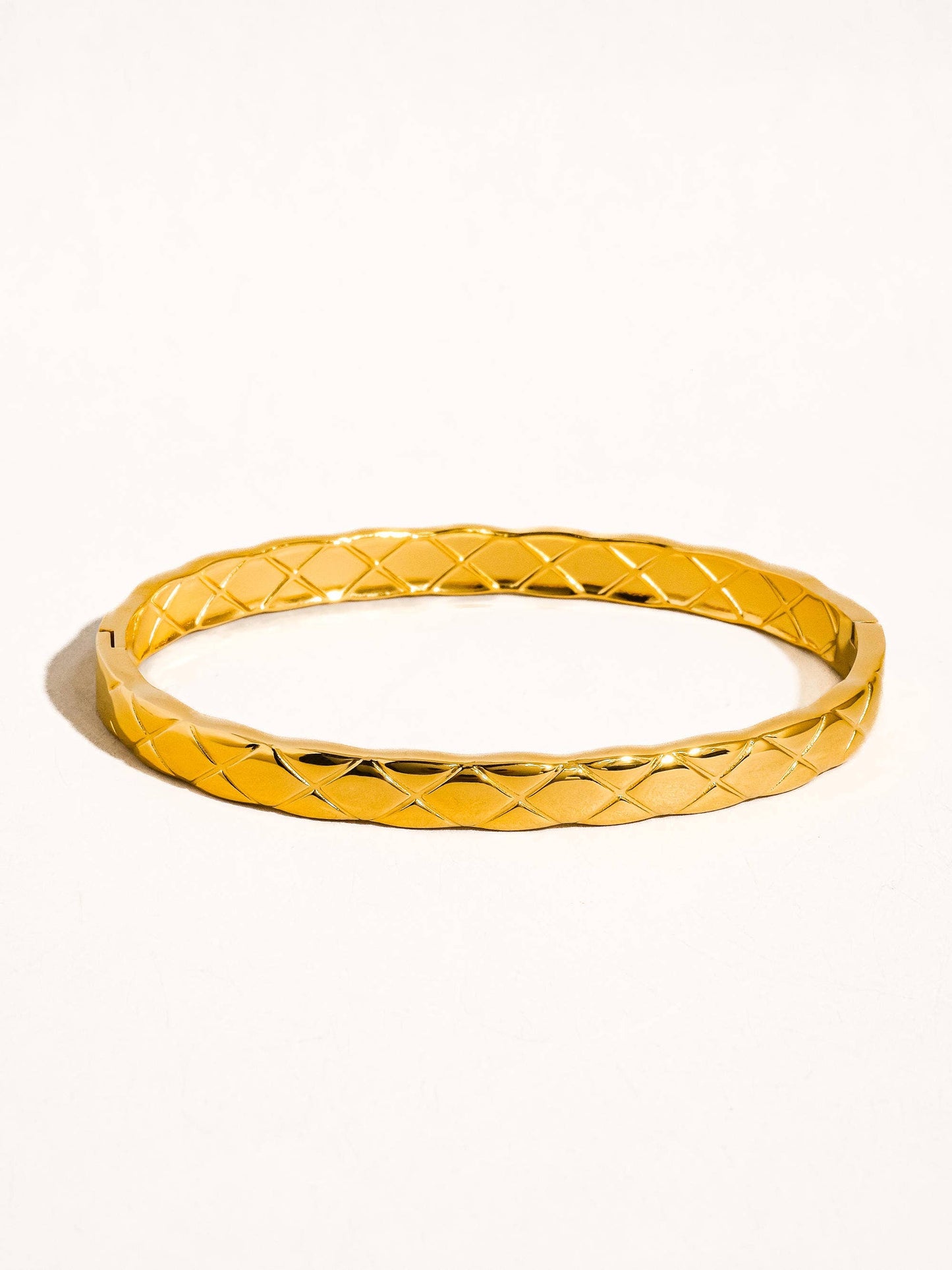Gold bangle with textured pattern on a white background