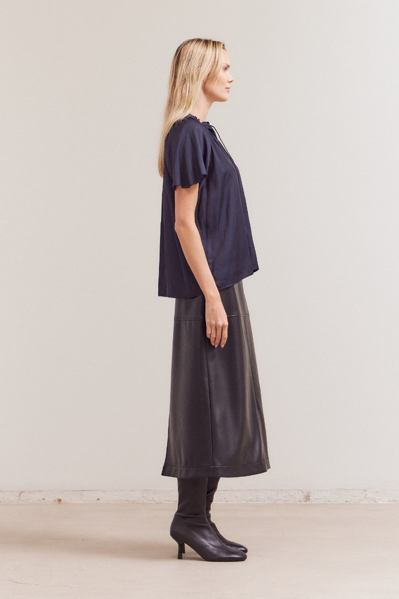 Woman wearing a dark blue top and black skirt against a plain background