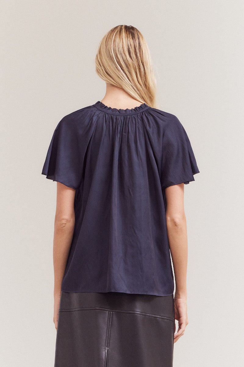 Person wearing a navy blue blouse with short sleeves on a plain background