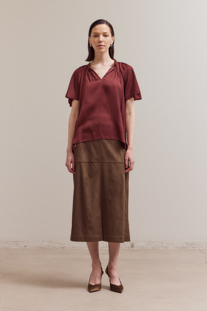 Woman wearing a rust-colored top and brown skirt against a plain background