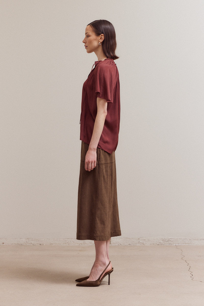 Woman wearing a burgundy top and brown skirt against a plain background