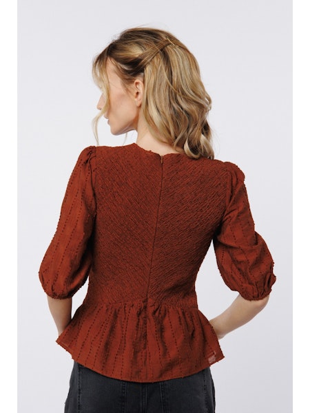Woman wearing a rust-colored textured blouse against a white background