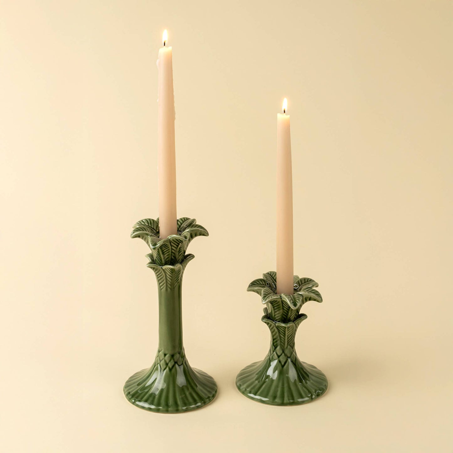 Two green ceramic candle holders with lit candles on a beige background