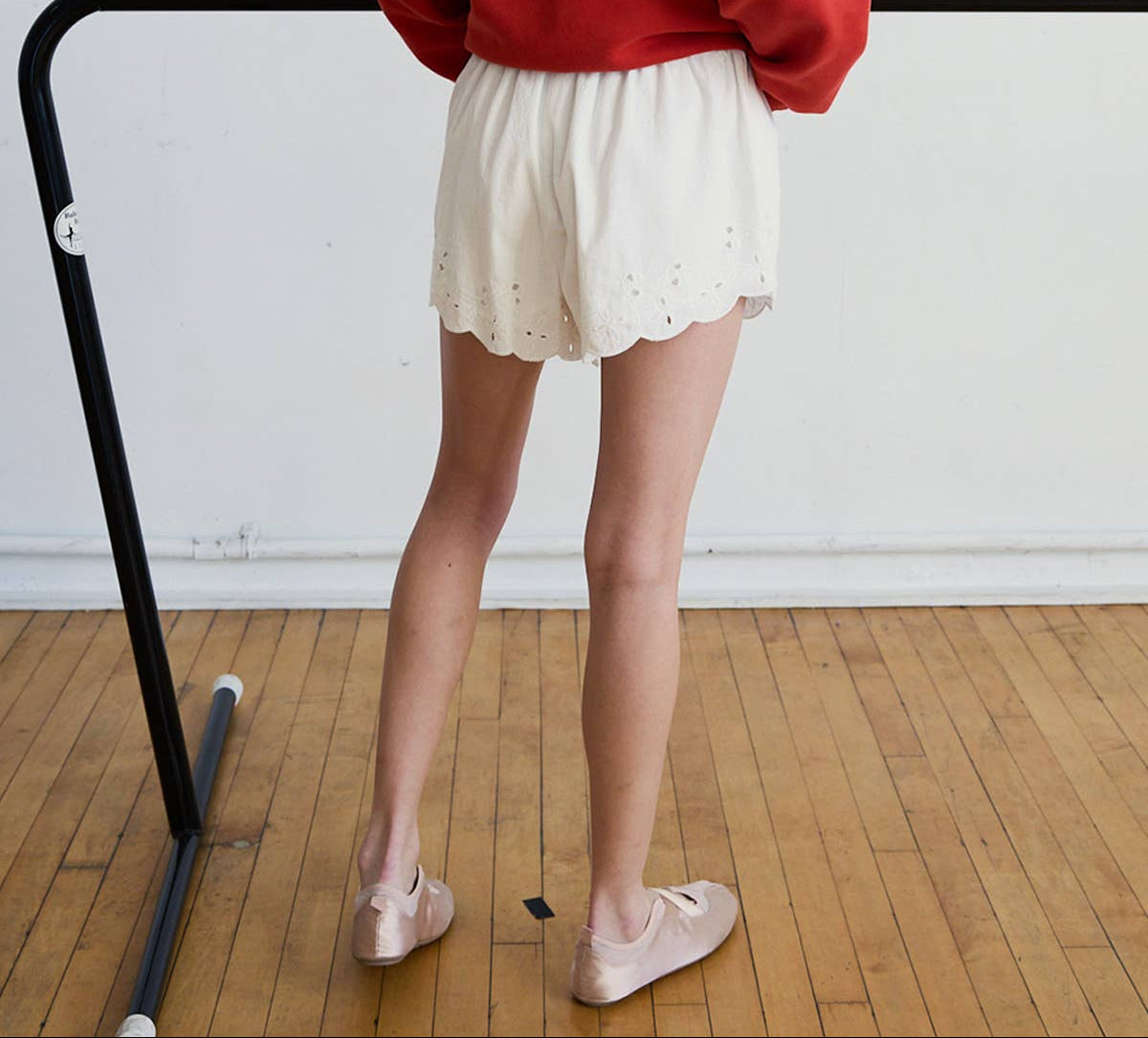 Woman wearing a red sweatshirt and white shorts standing in a dance studio.