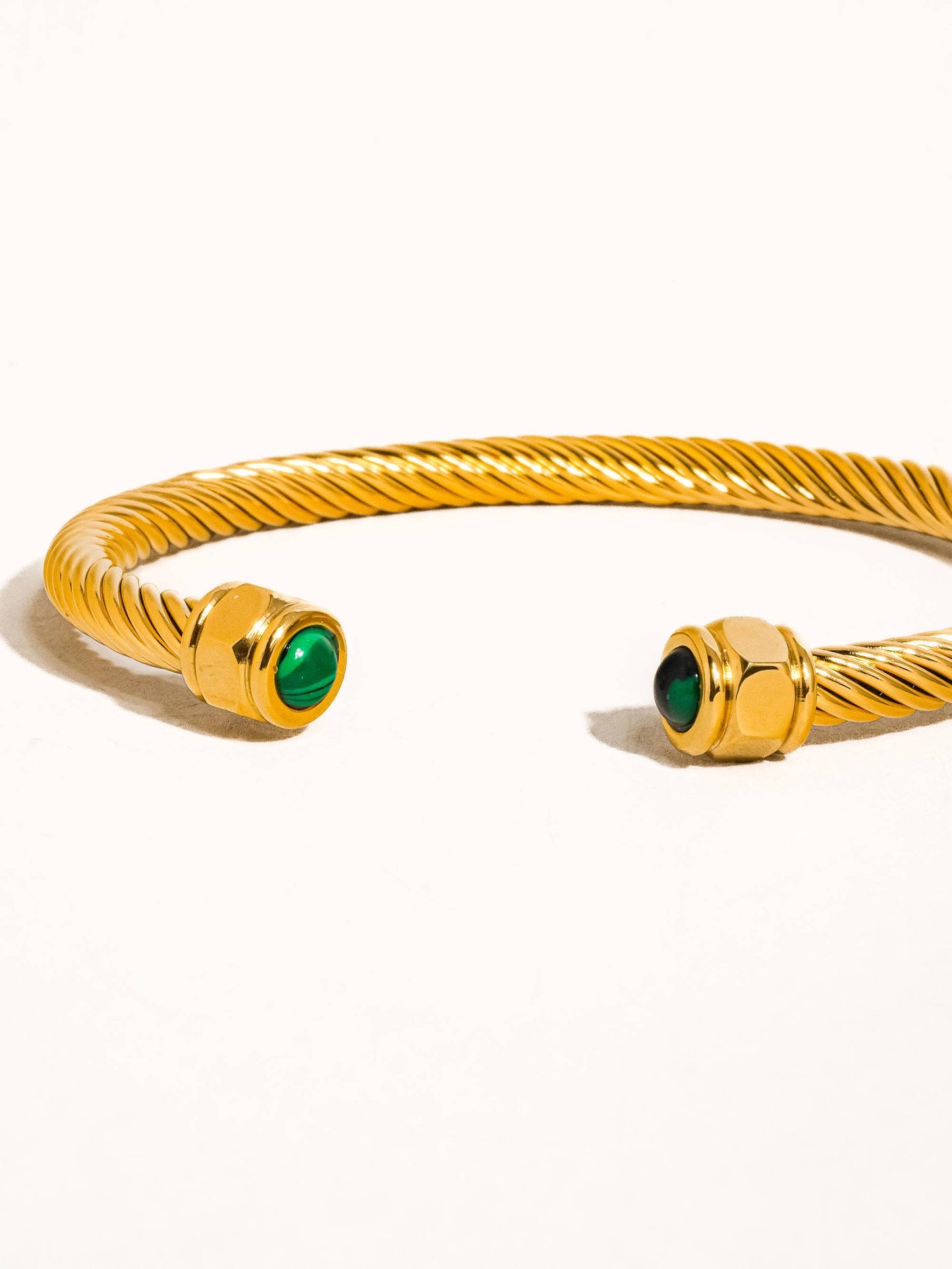 Gold bracelet with green gemstones on a white background