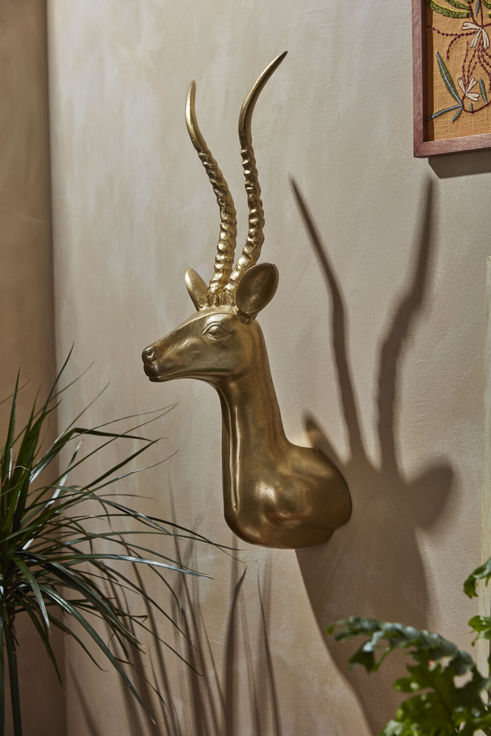 Gold antelope head wall decoration on a beige wall with plants around