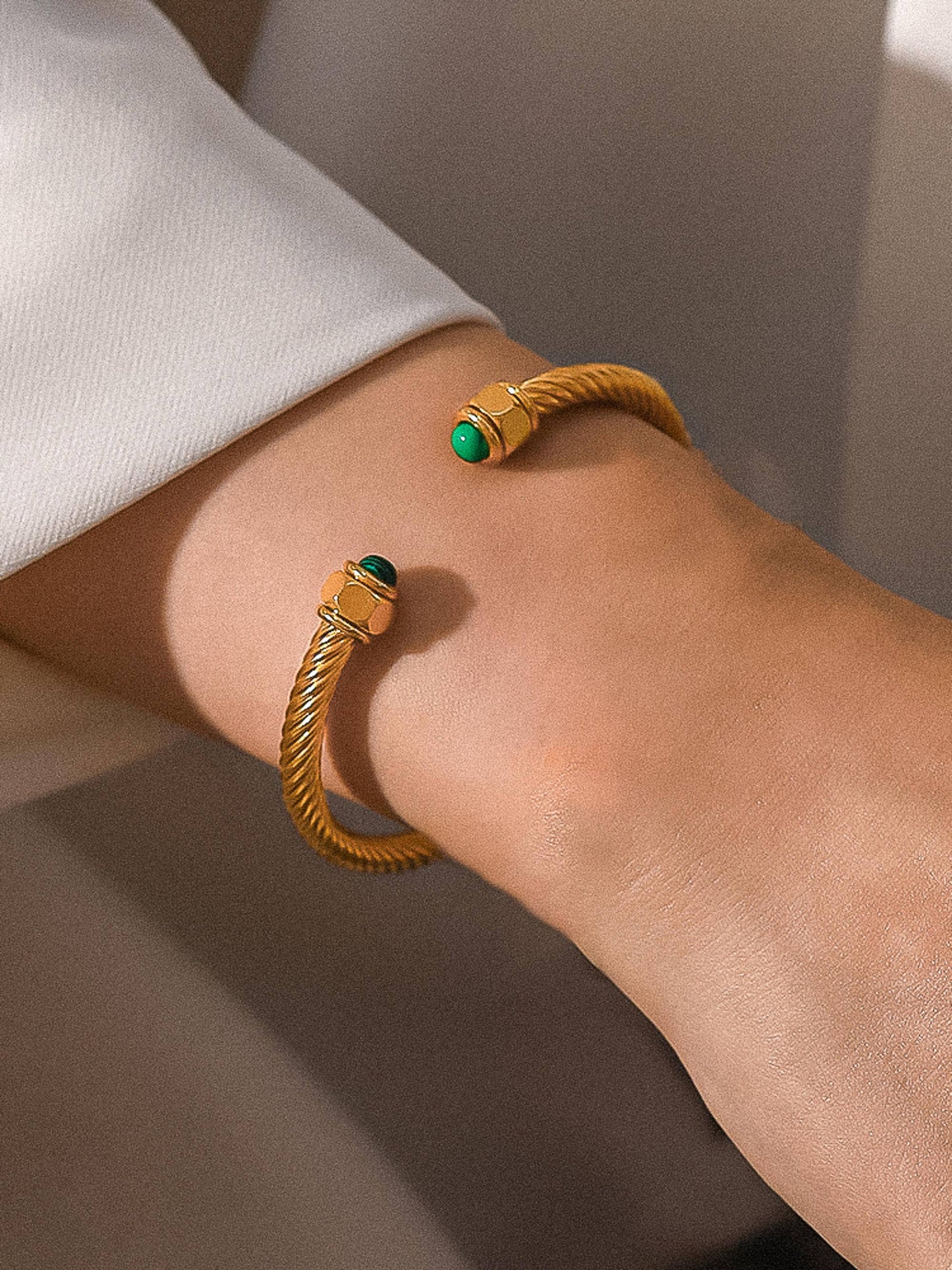 Gold bracelet with green gemstones on a wrist against a neutral background