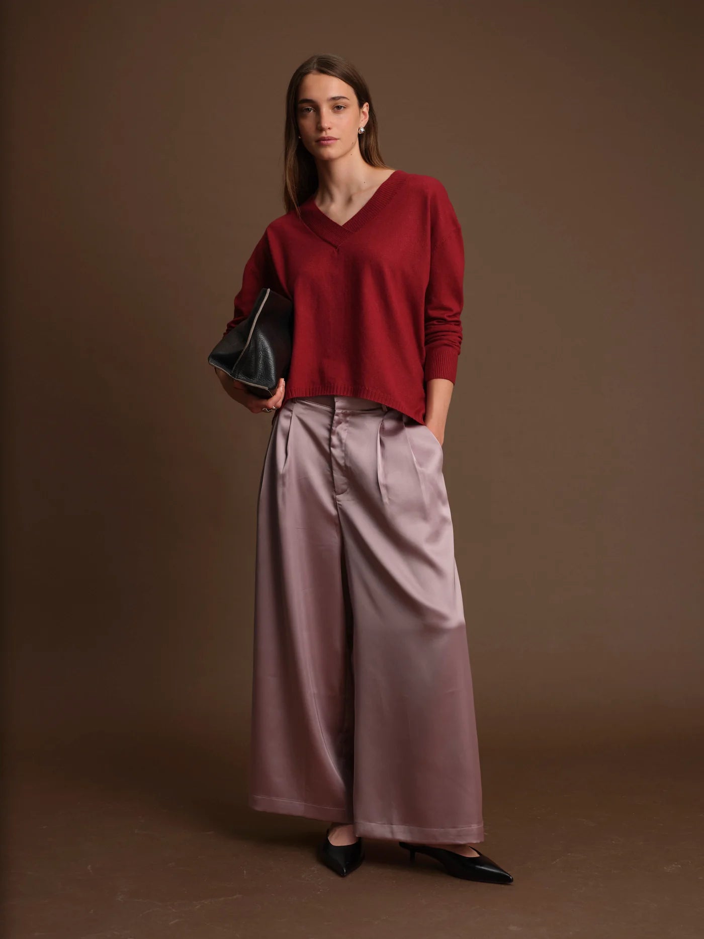 Woman wearing a red sweater and pink pants against a brown background