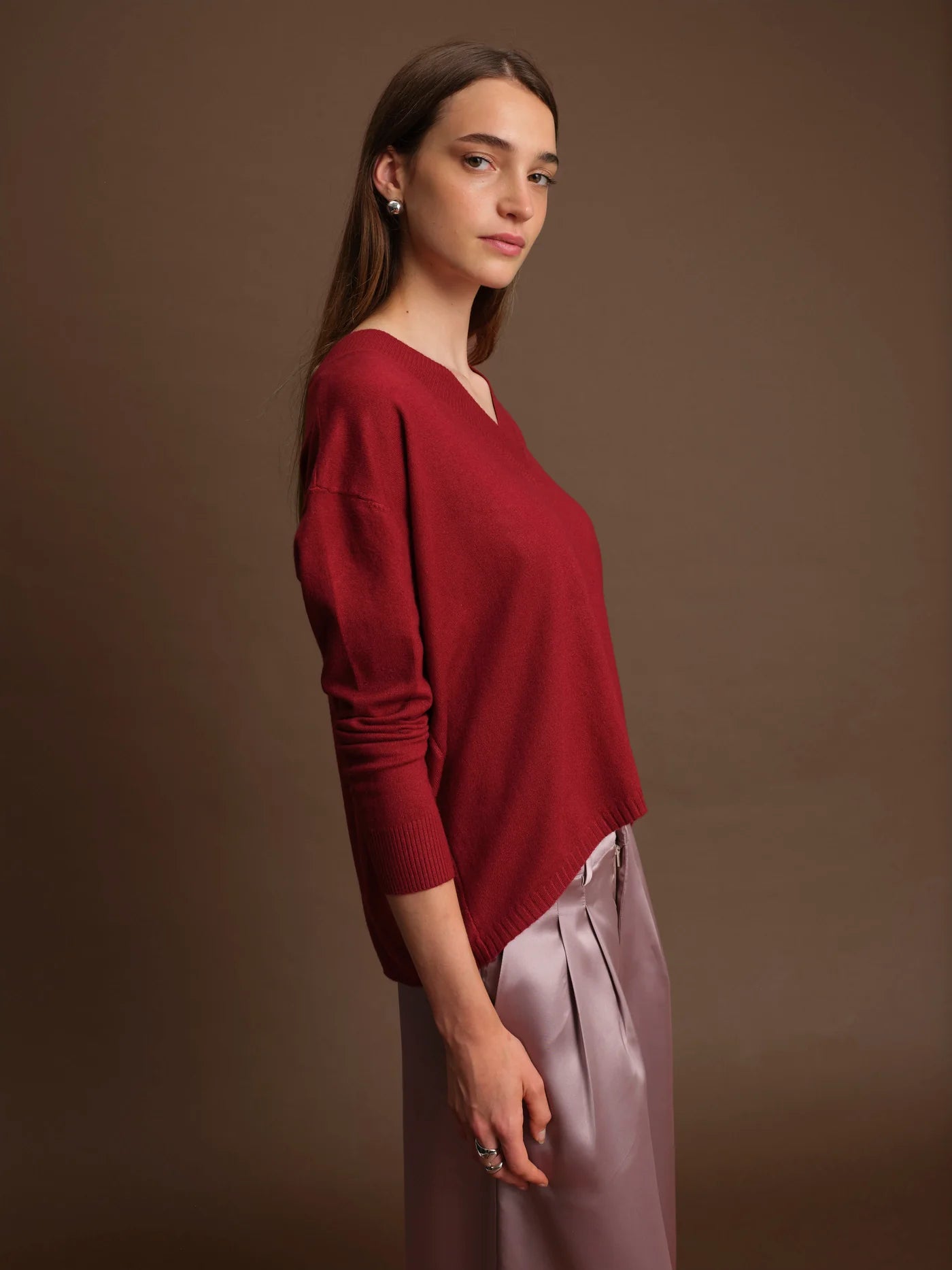 Woman wearing a red sweater and light purple pants against a brown background