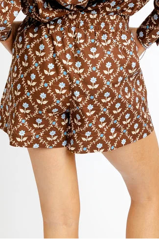 A woman wearing brown and blue floral shorts standing against a plain white studio background.