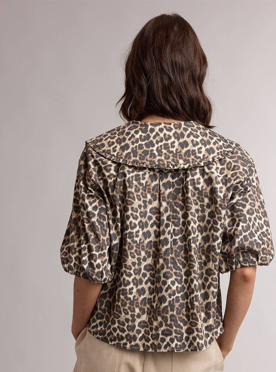 Person wearing a leopard print jacket and beige pants on a plain background