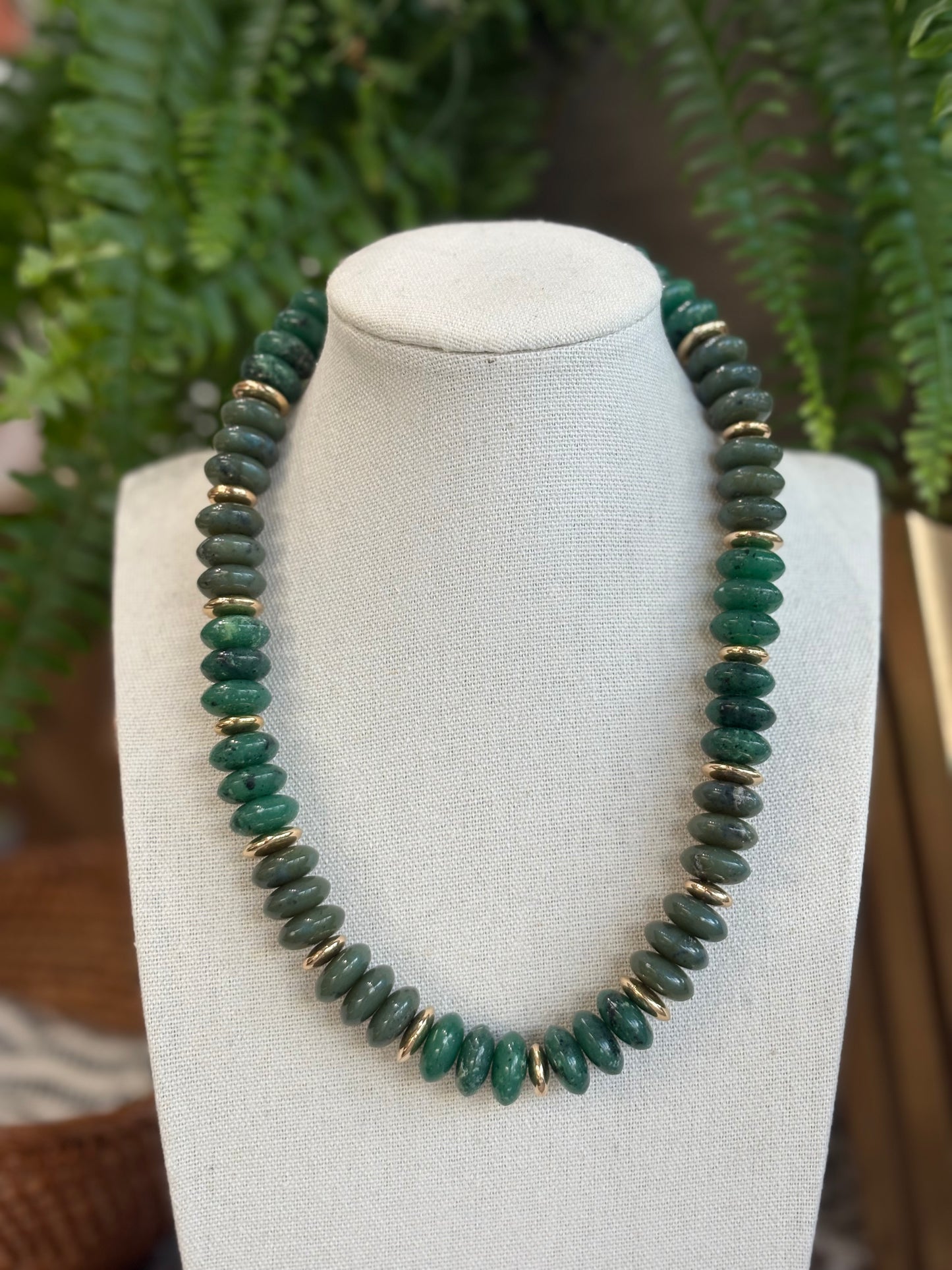 Green beaded necklace on a mannequin bust with a fern background