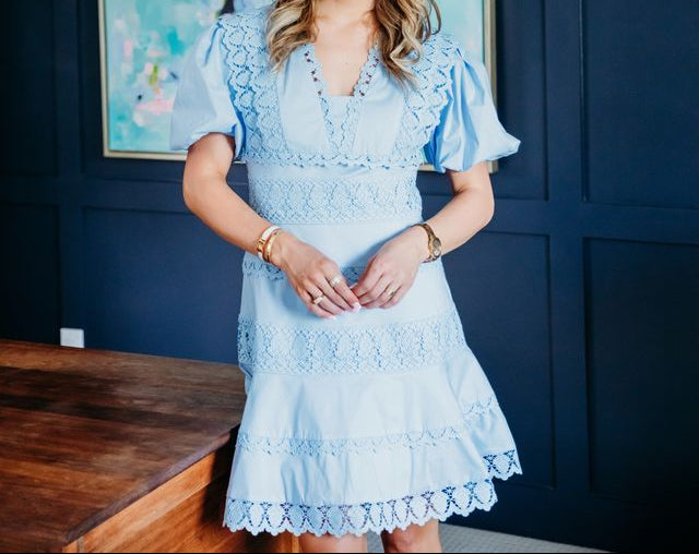 Woman in a light blue dress standing in a room with a blue wall and a painting.