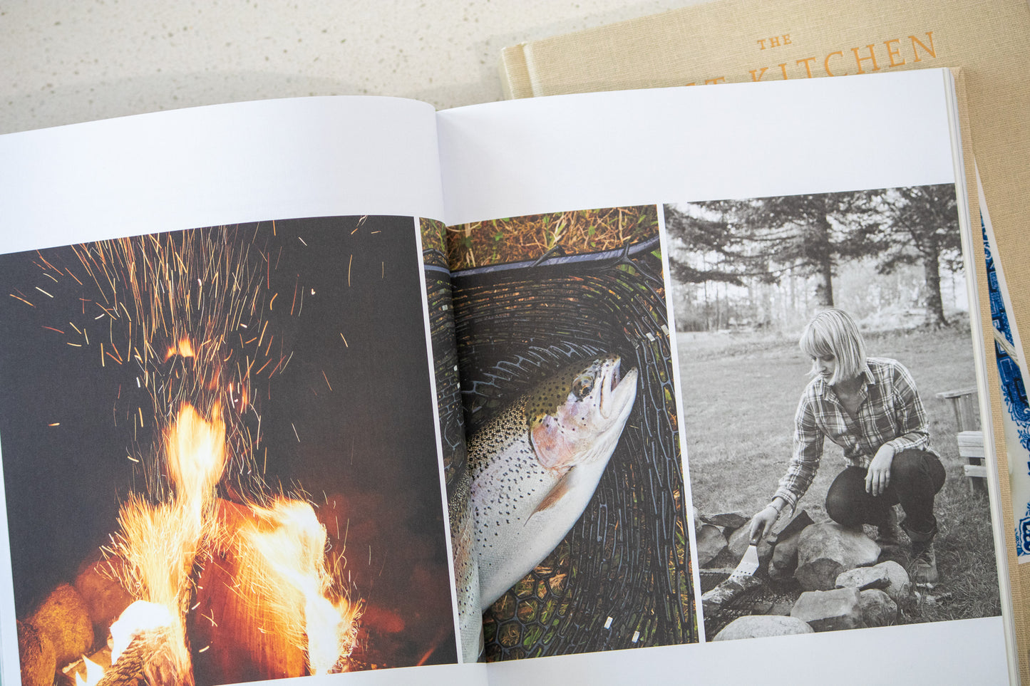 Open book showing images of a fire, fish, and a person by a lake.
