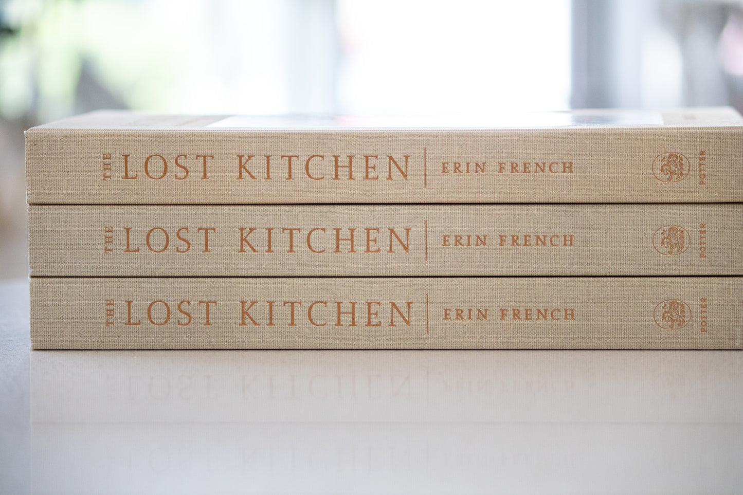 Three copies of 'The Lost Kitchen' by Erin French stacked on a light surface with a blurred background.