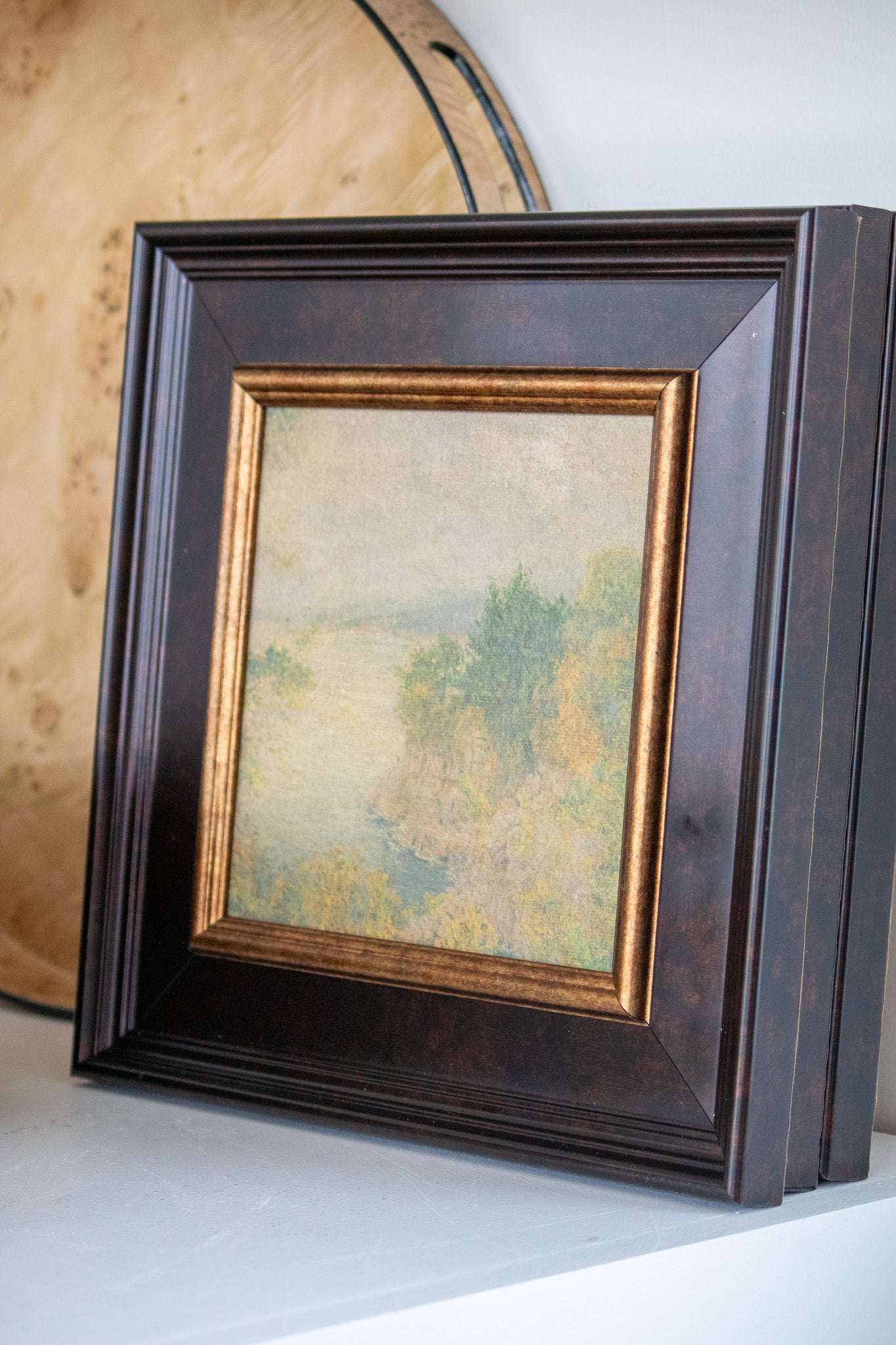 Framed artwork with a natural scene inside, on a white surface.