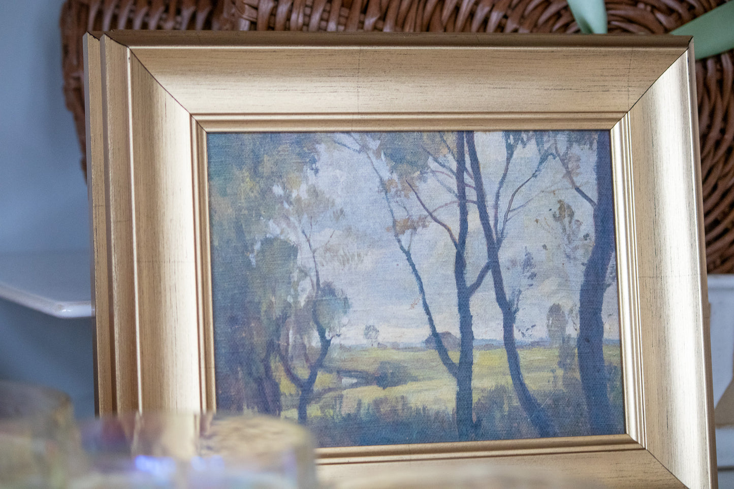 Framed painting of a landscape with trees and a field.