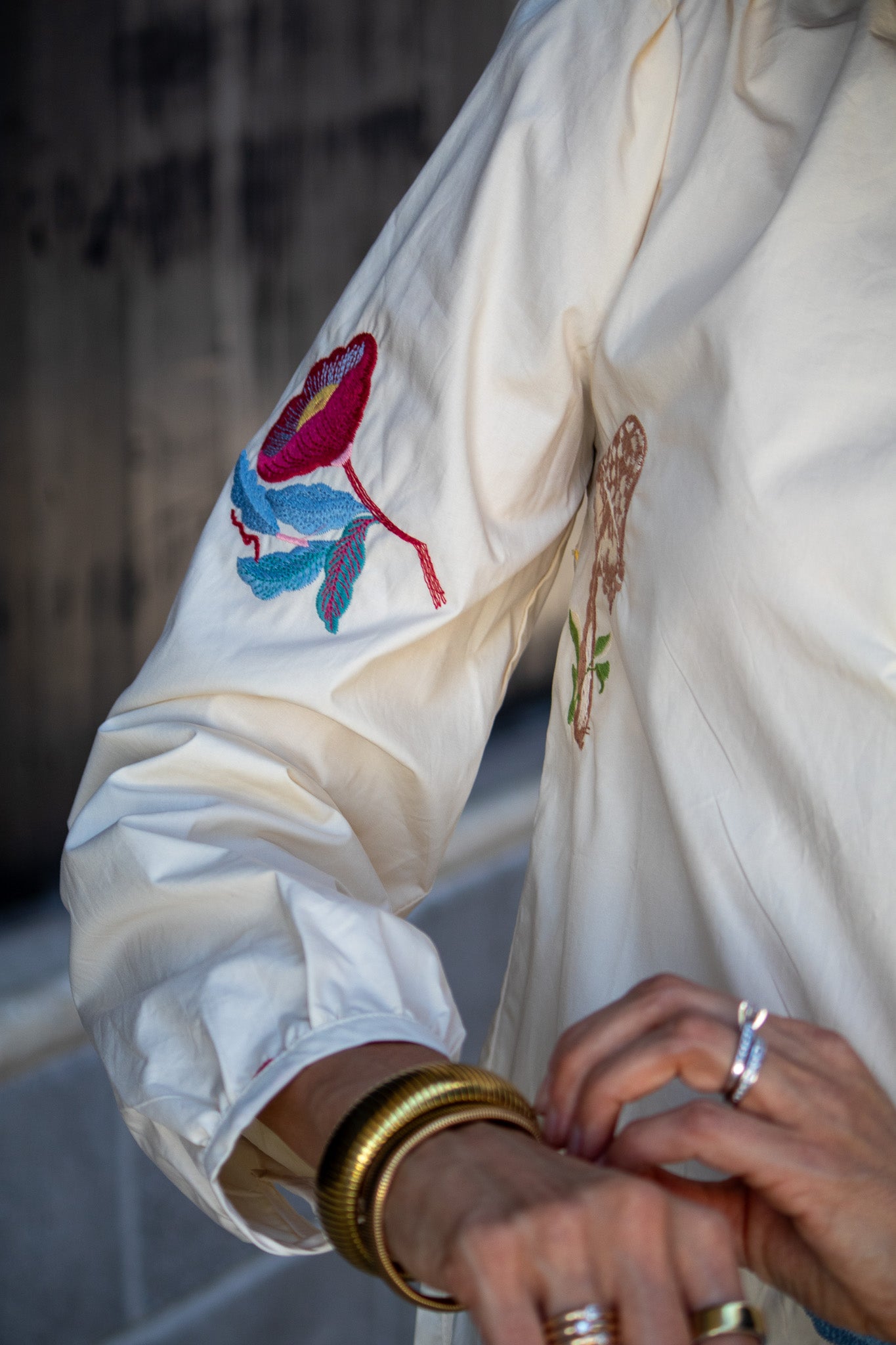 Close-up of a white embroidered garment with colorful floral designs, worn by a person with gold bangles.