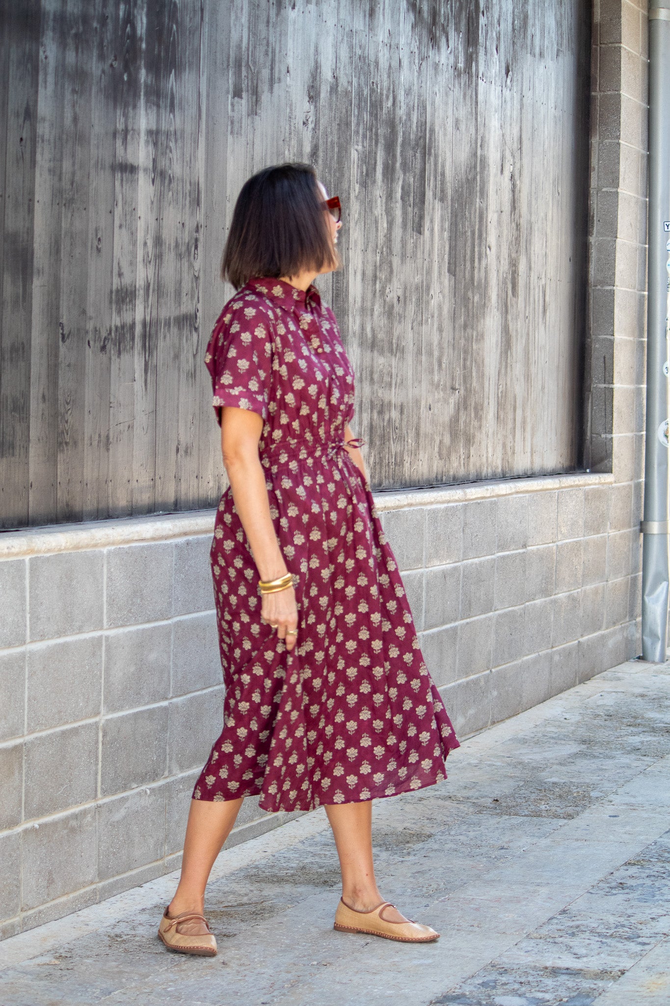 Woman in a maroon patterned dress standing against a textured wall.