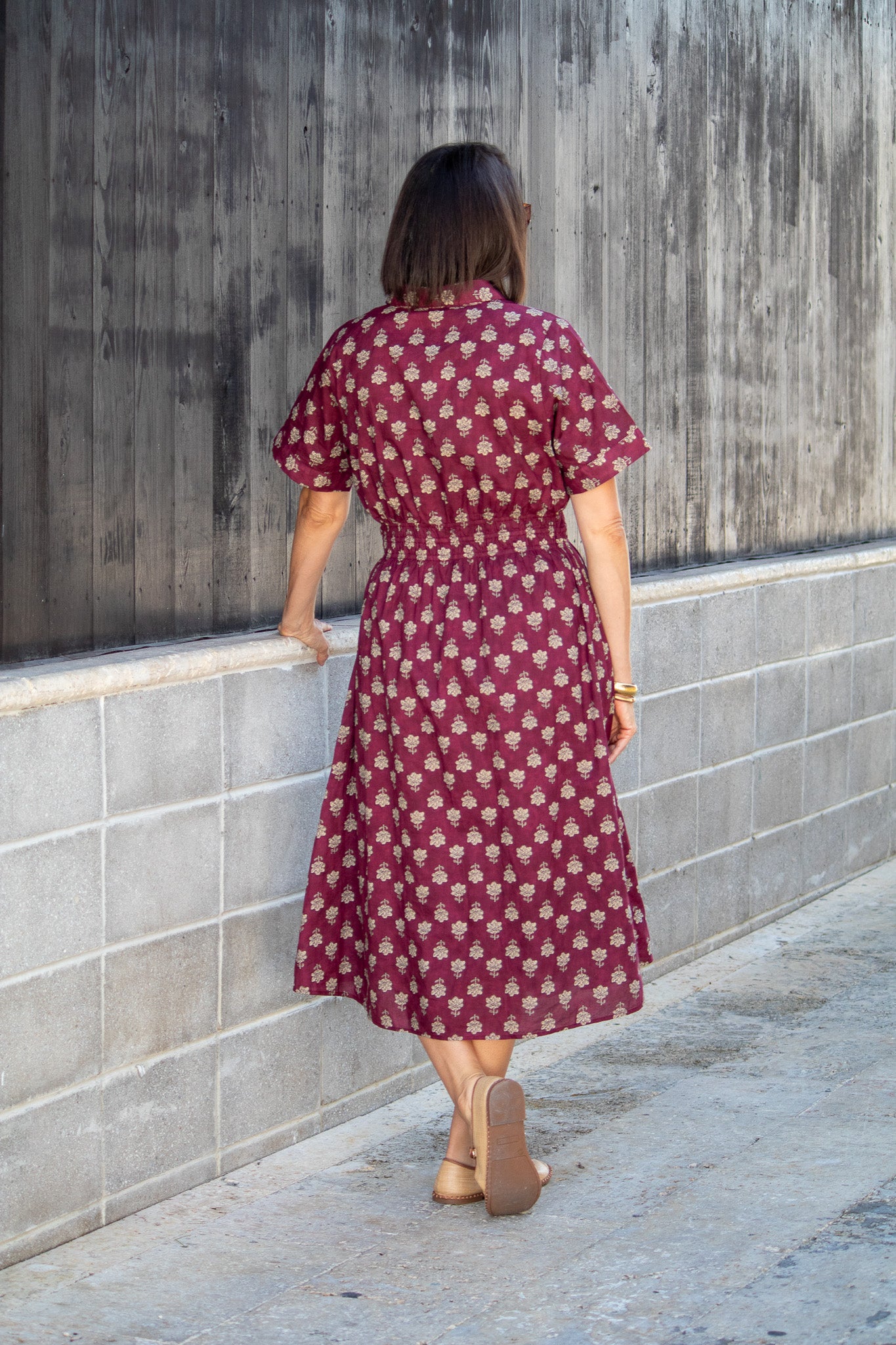Woman wearing a maroon dress with white floral pattern against a concrete wall.