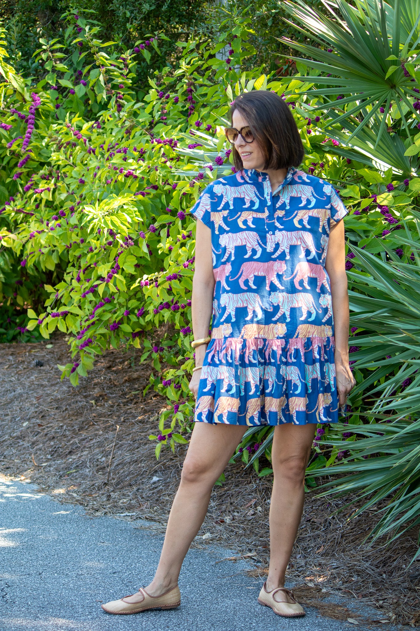 Woman wearing a blue dress with animal pattern standing outdoors among greenery