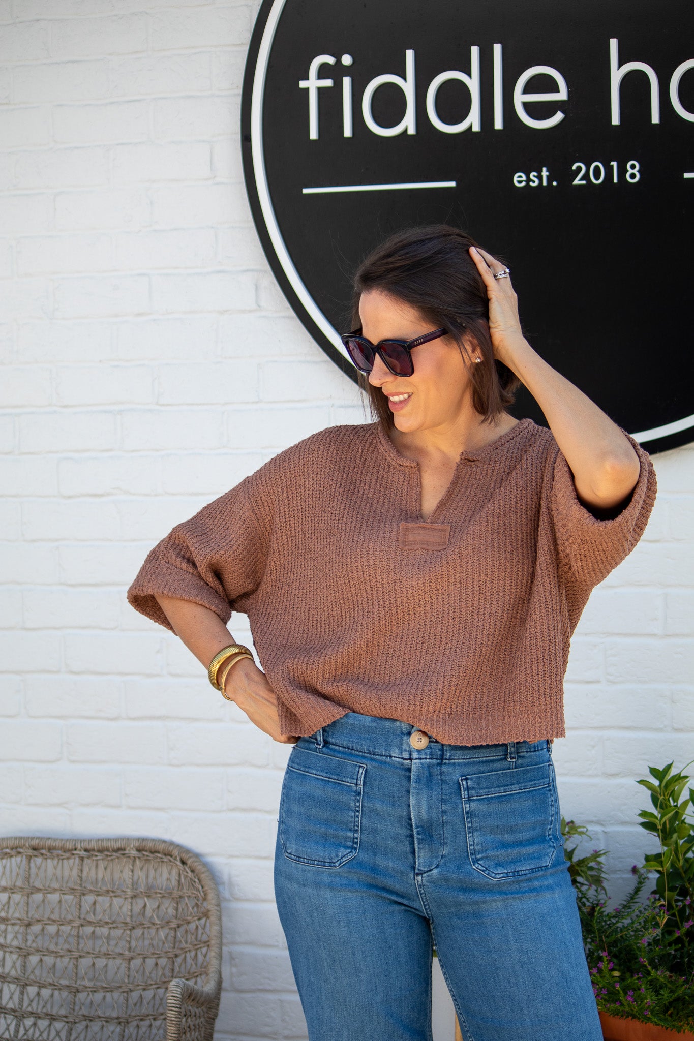 Woman posing in front of a 'fiddle haus' sign with a white brick wall background