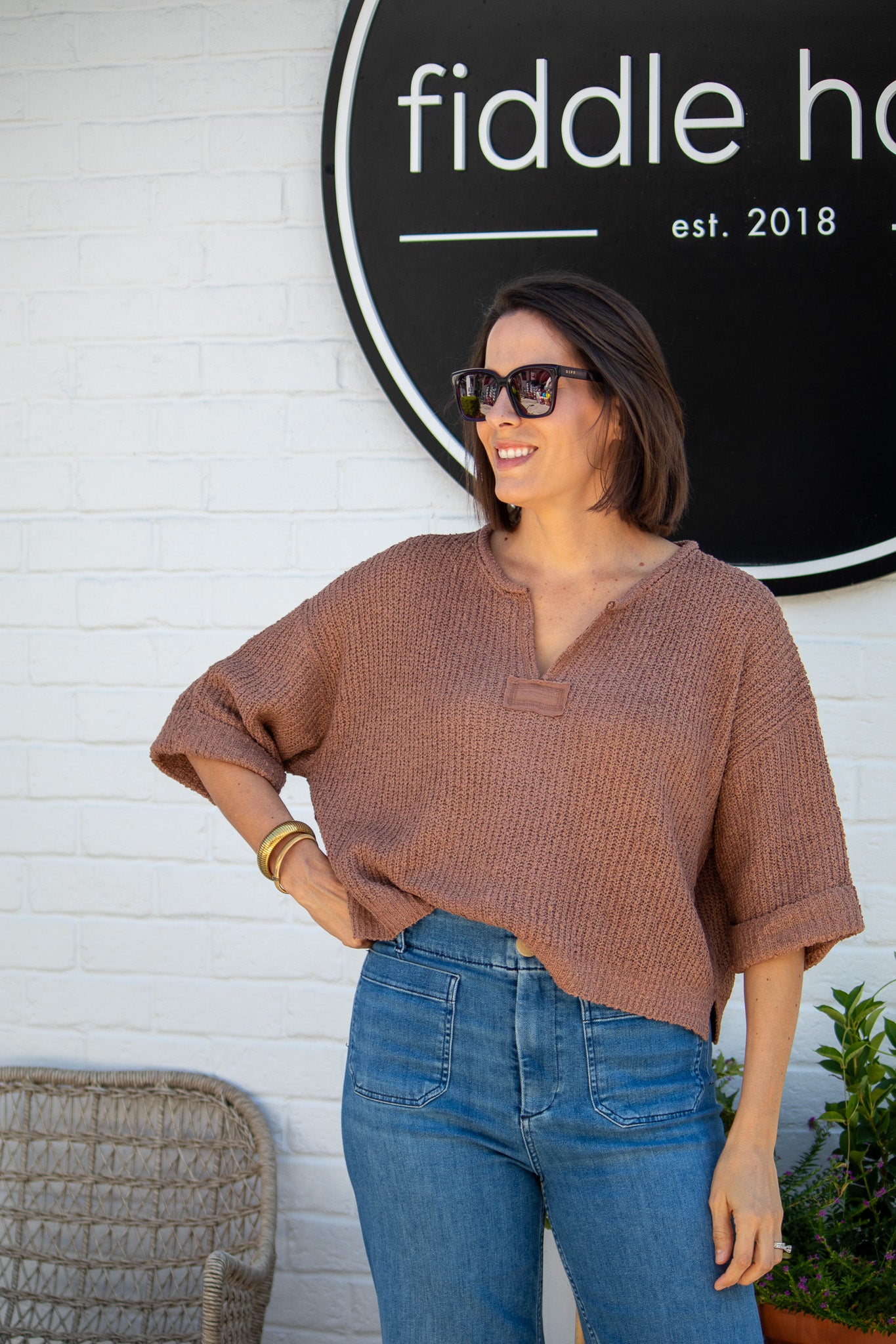 Woman wearing sunglasses and a brown top in front of a 'fiddle haus' sign.