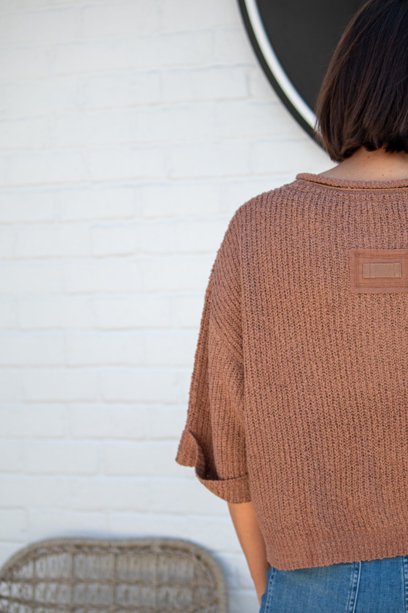 Person wearing a brown textured sweater against a white brick wall.
