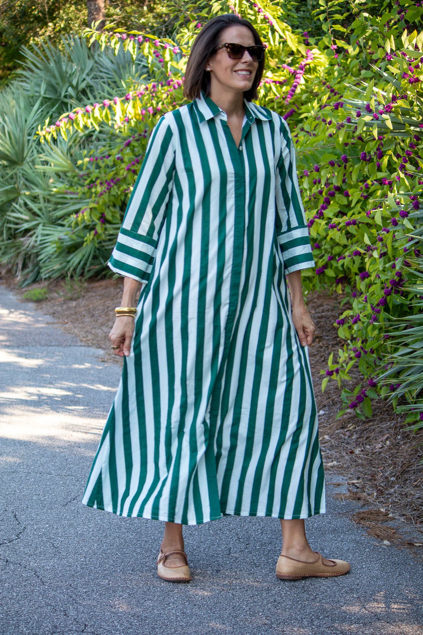 Woman wearing a green and white striped dress standing on a path with greenery in the background