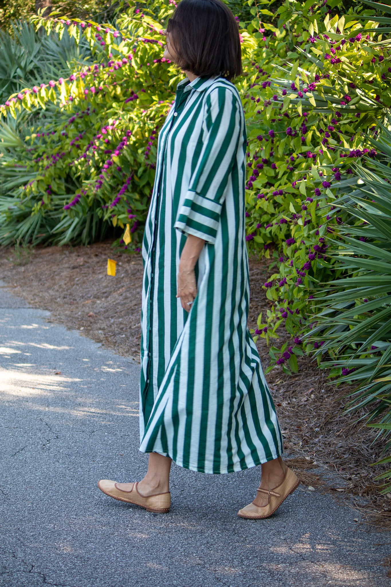 Woman in a green and white striped dress standing on a path with plants in the background