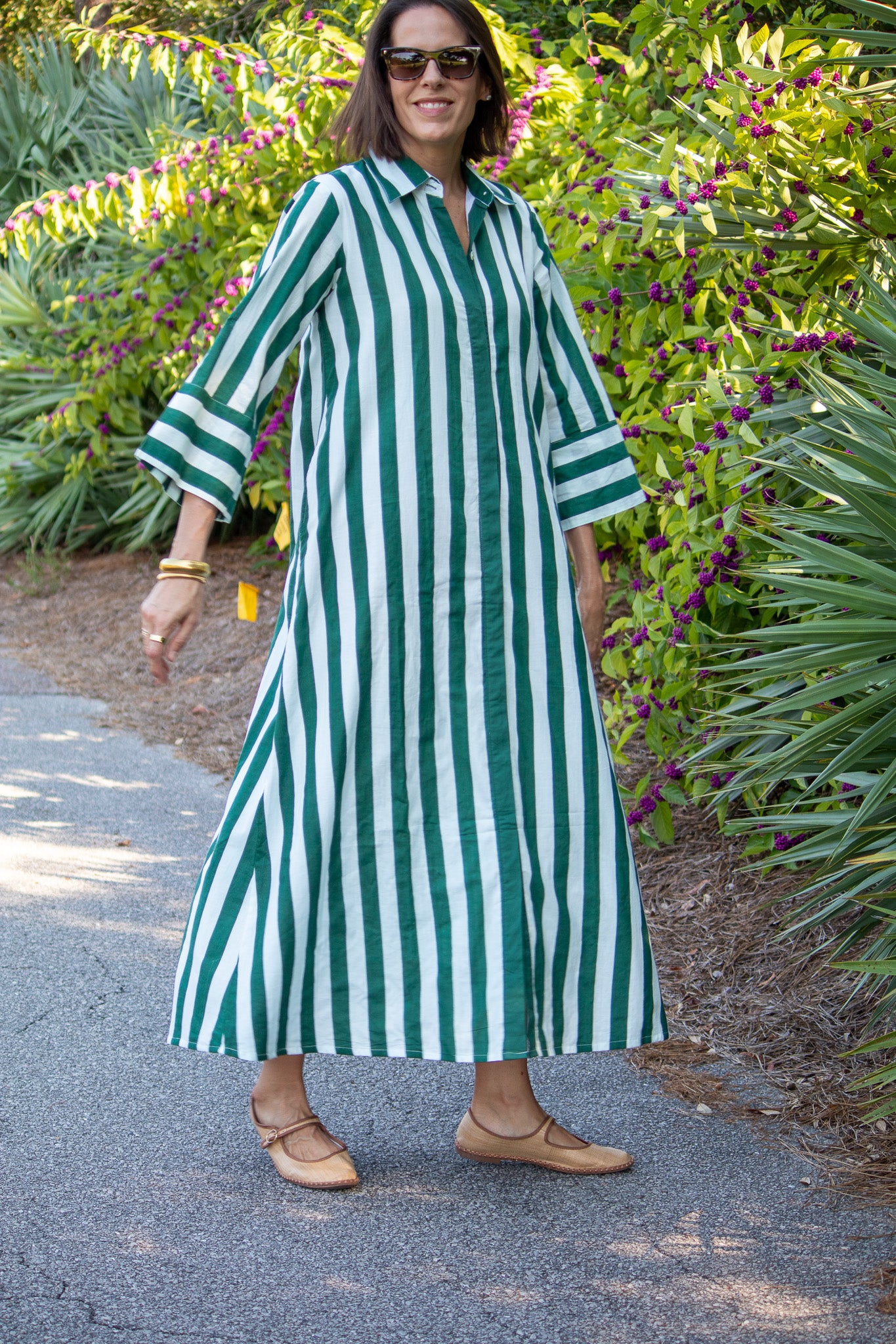 Woman wearing a green and white striped dress standing in a garden.
