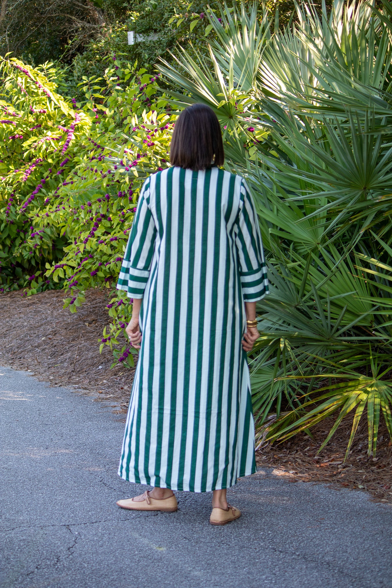 Person wearing a green and white striped dress walking on a path with plants in the background