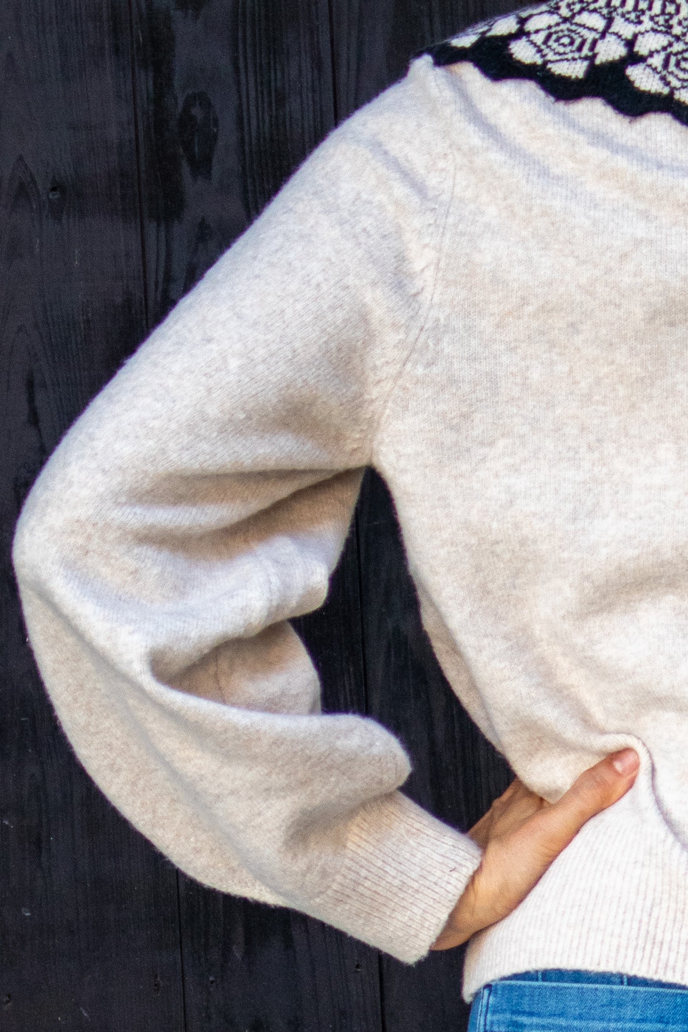 Close-up of a person wearing a tan sweater with a dark background