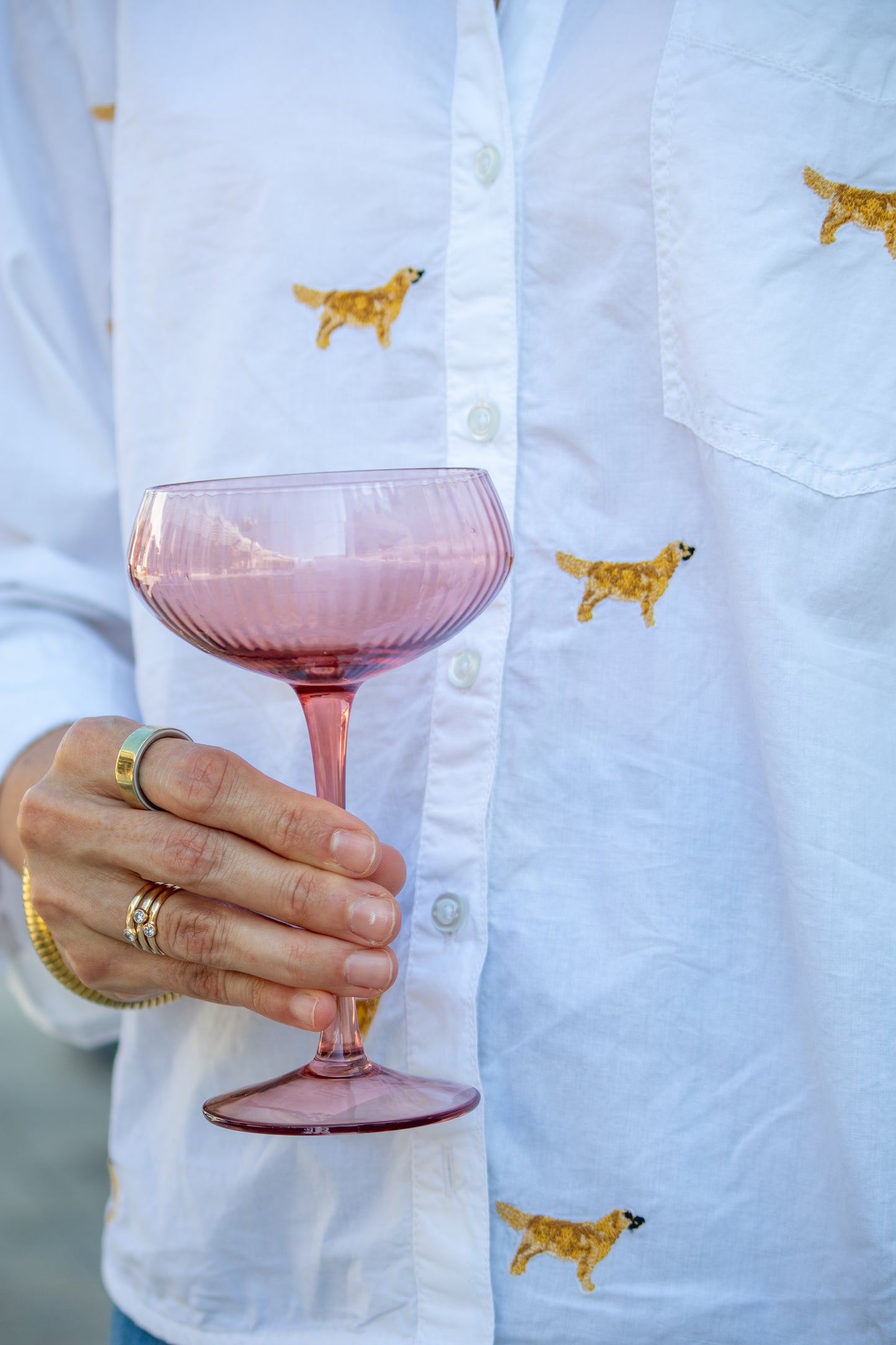 Person holding a pink glass with a white shirt featuring dog embroidery.