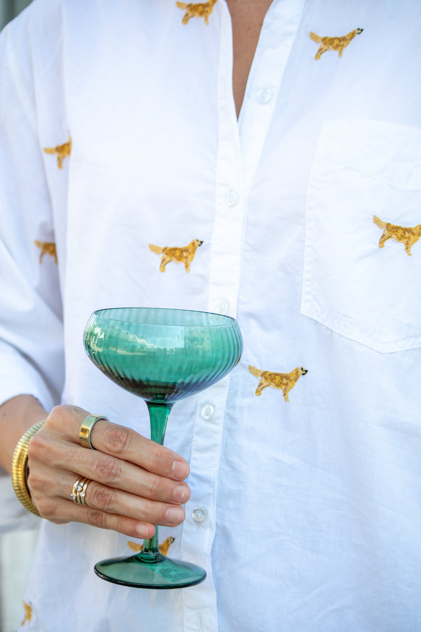 Person holding a green cocktail glass with a white shirt featuring small dog patterns.