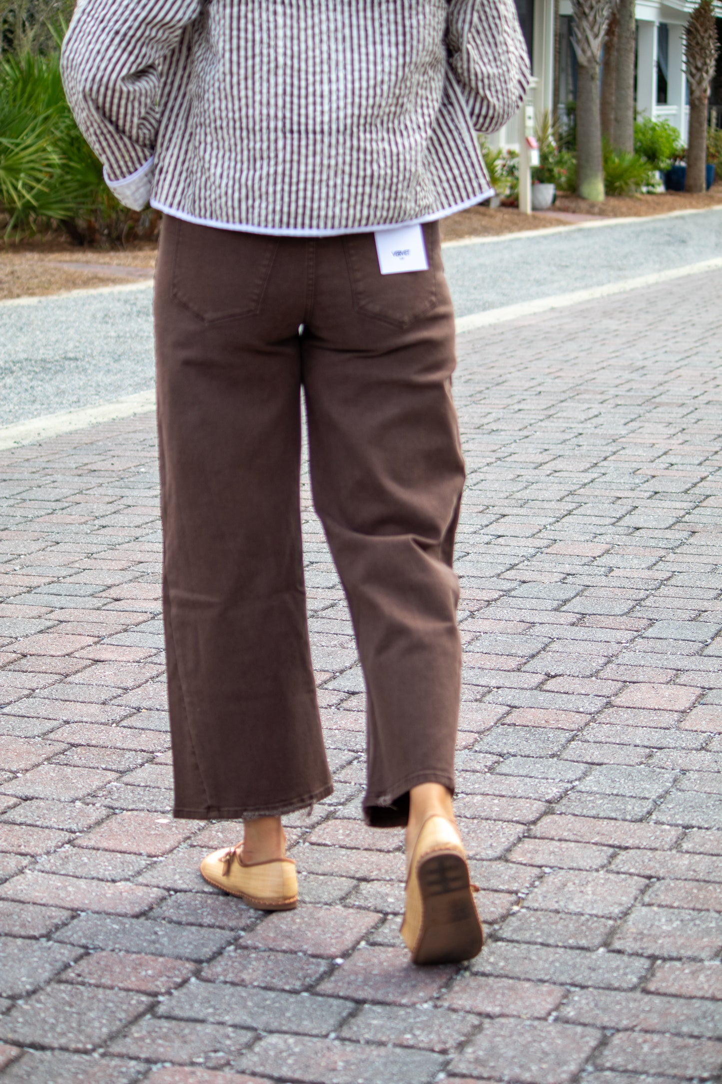 Person wearing brown pants and a checkered shirt on a paved walkway.