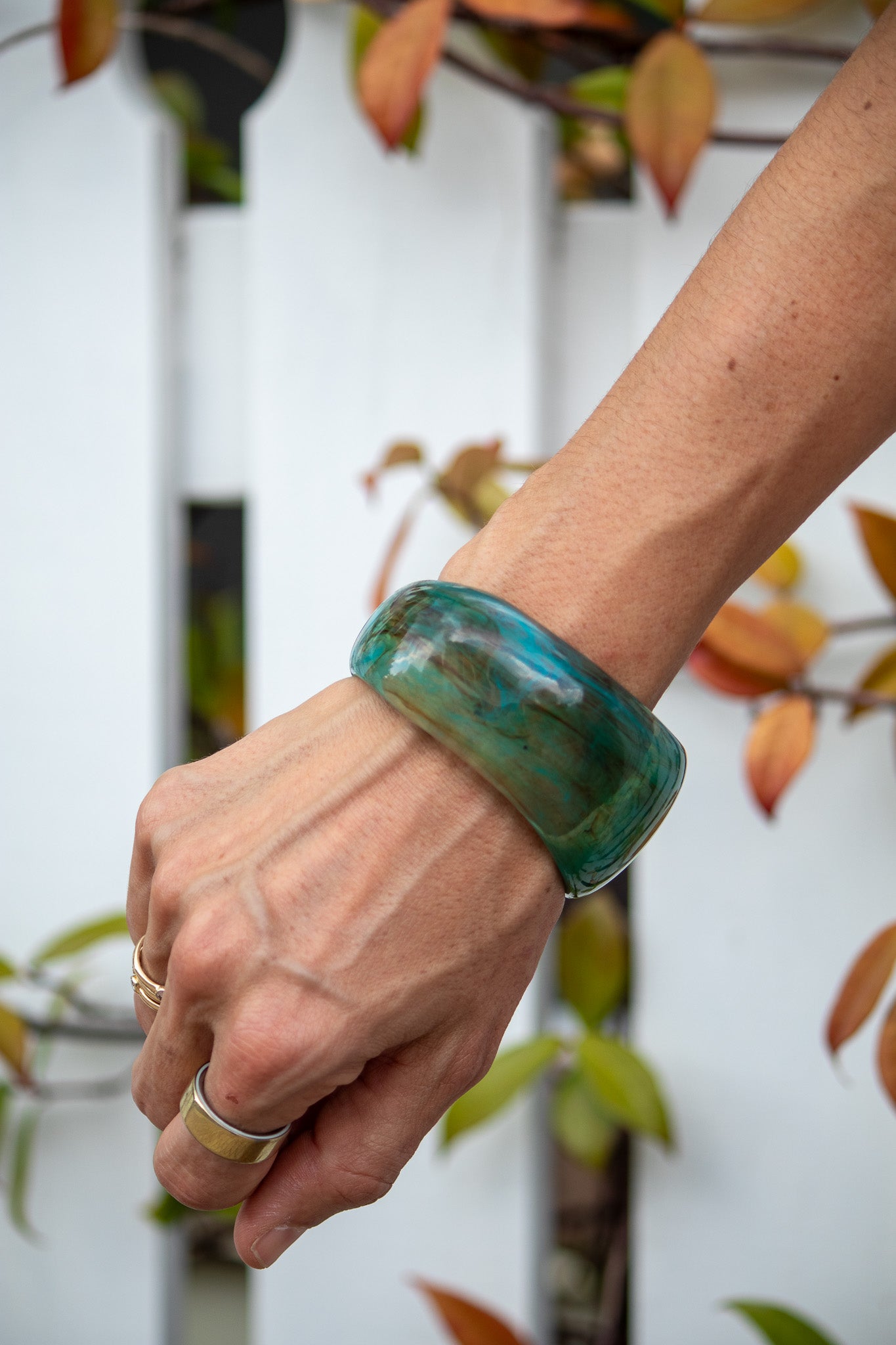 Hand wearing a green bracelet with a blurred natural background