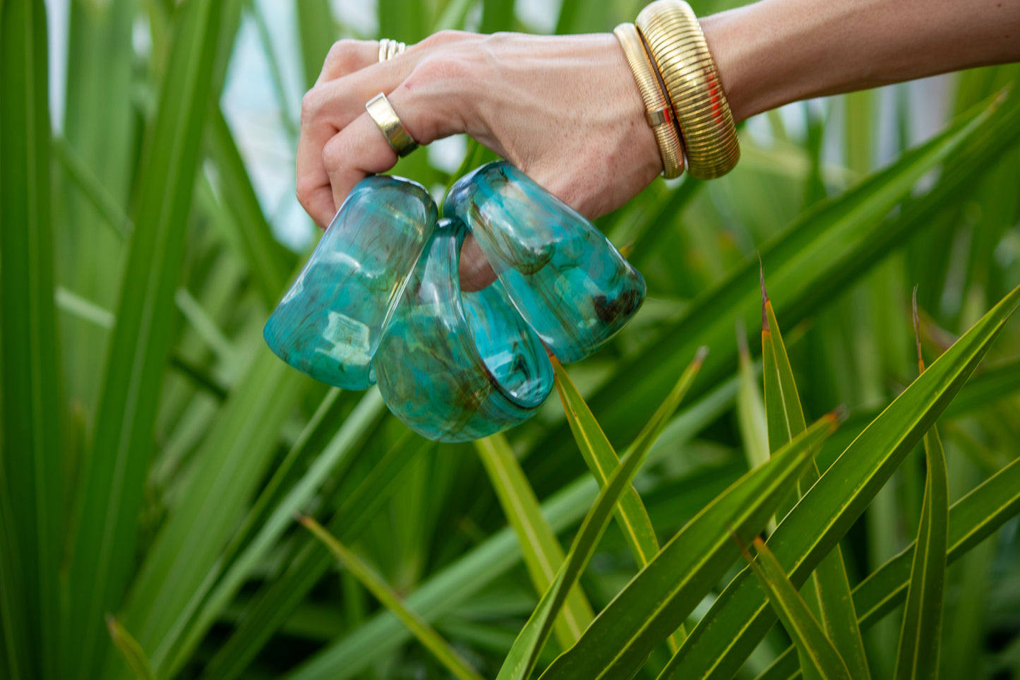 Hand holding three green bangles against a green leafy background