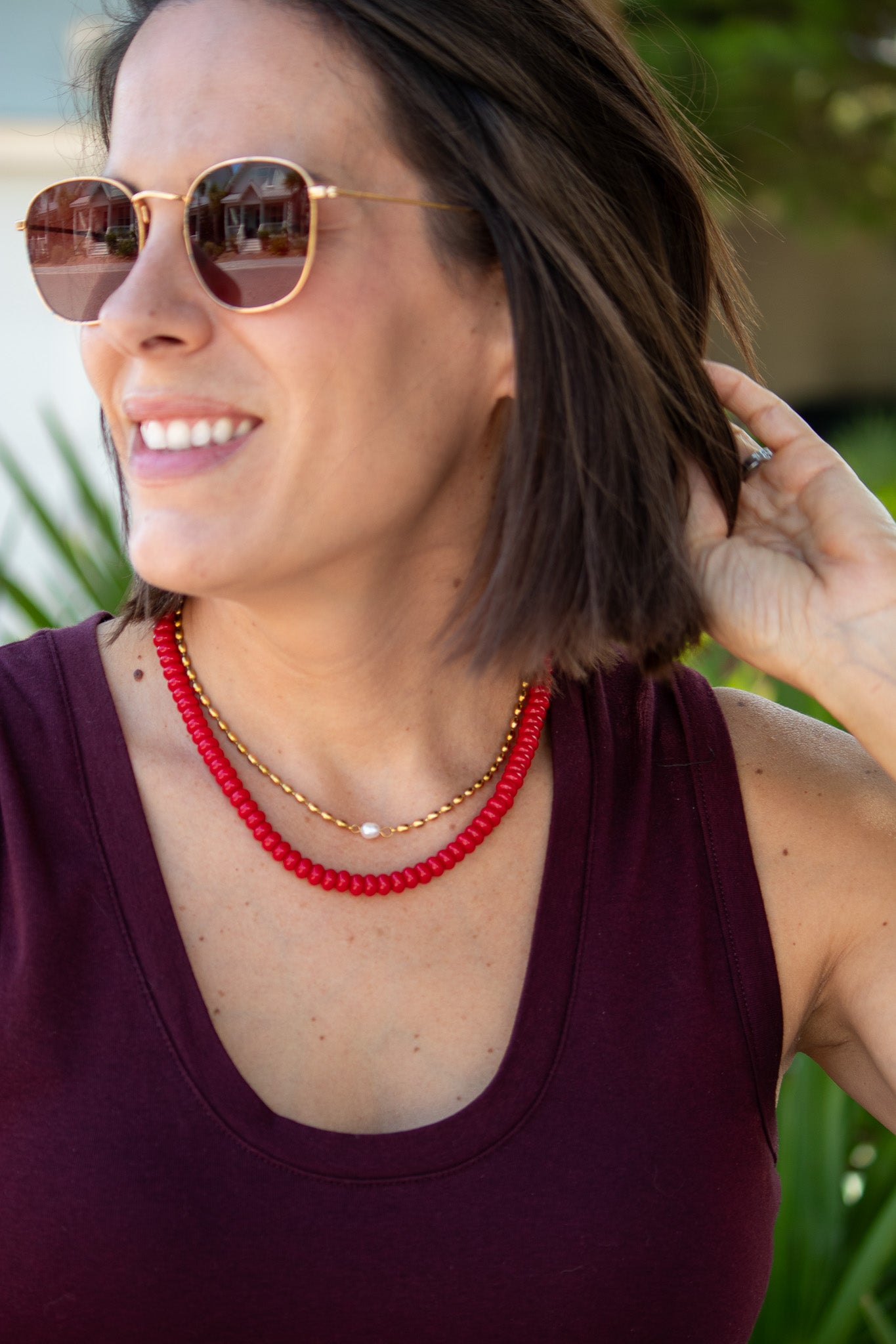 Woman wearing sunglasses and a red beaded necklace with a blurred green background