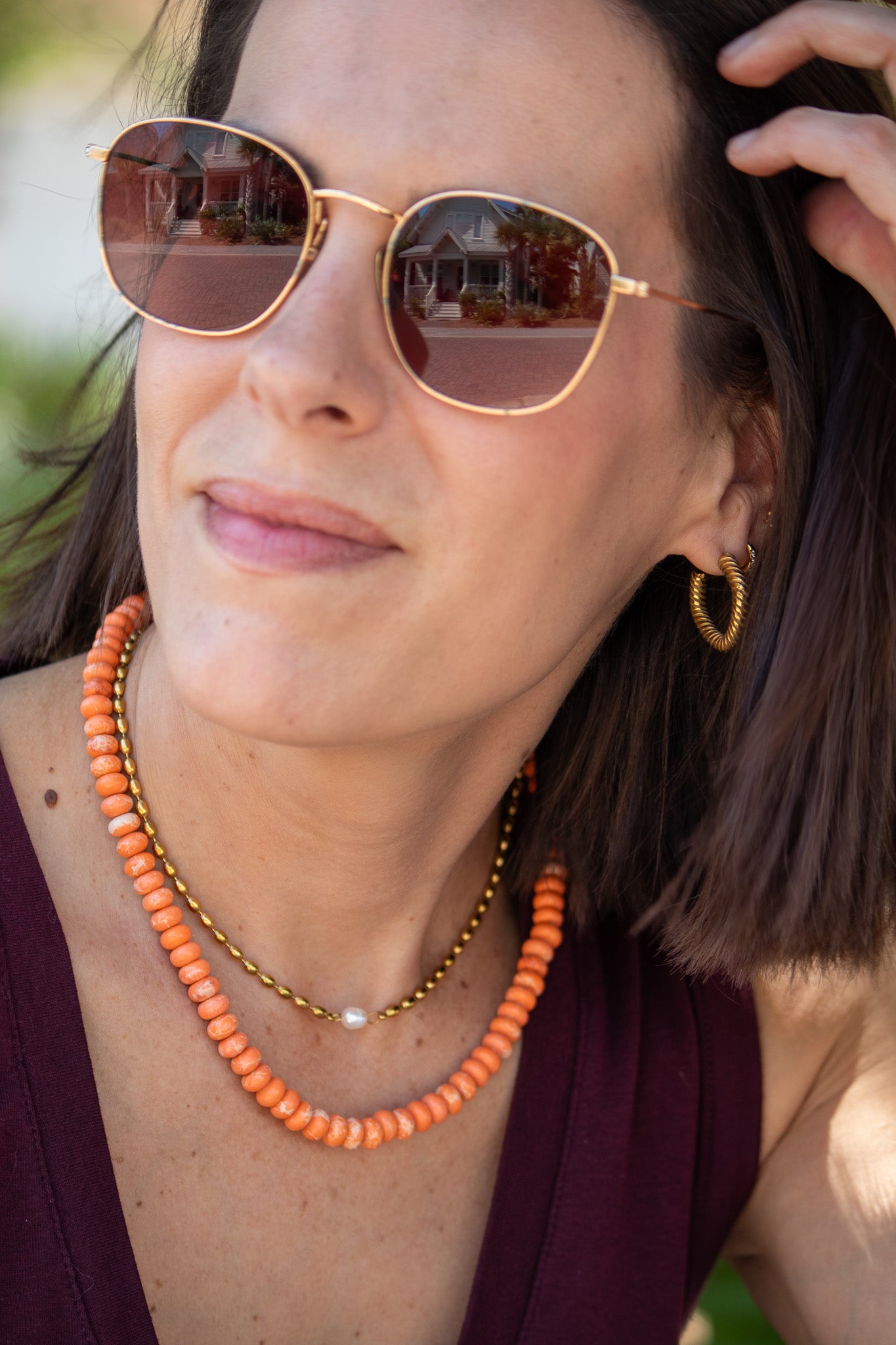 Woman wearing sunglasses and an orange beaded necklace with a blurred background