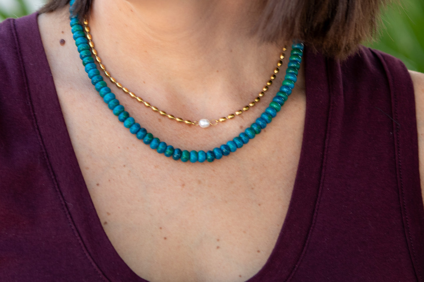 Close-up of a person wearing a turquoise beaded necklace with a gold chain.