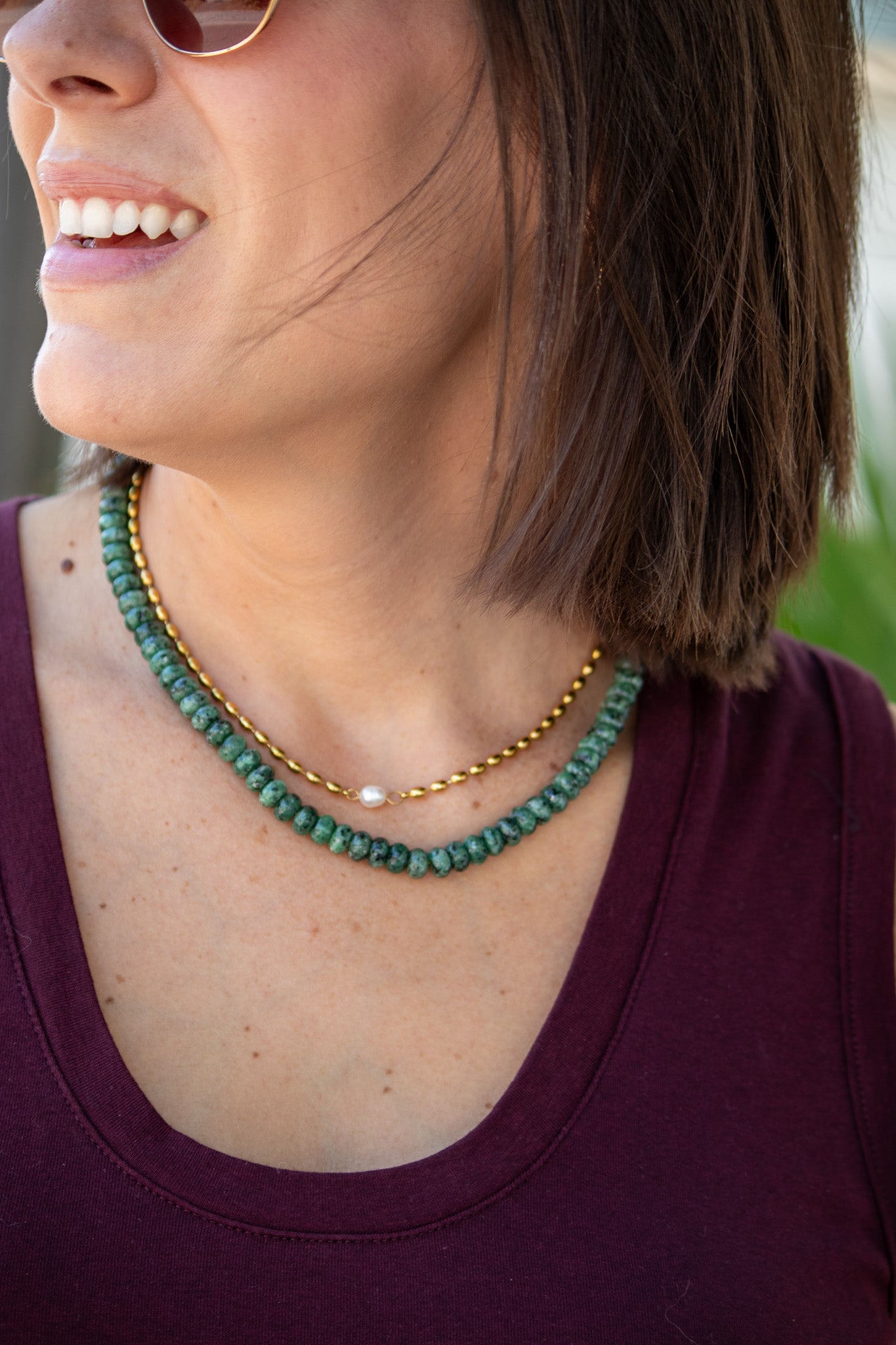 Close-up of a woman wearing a green beaded necklace with a blurred background