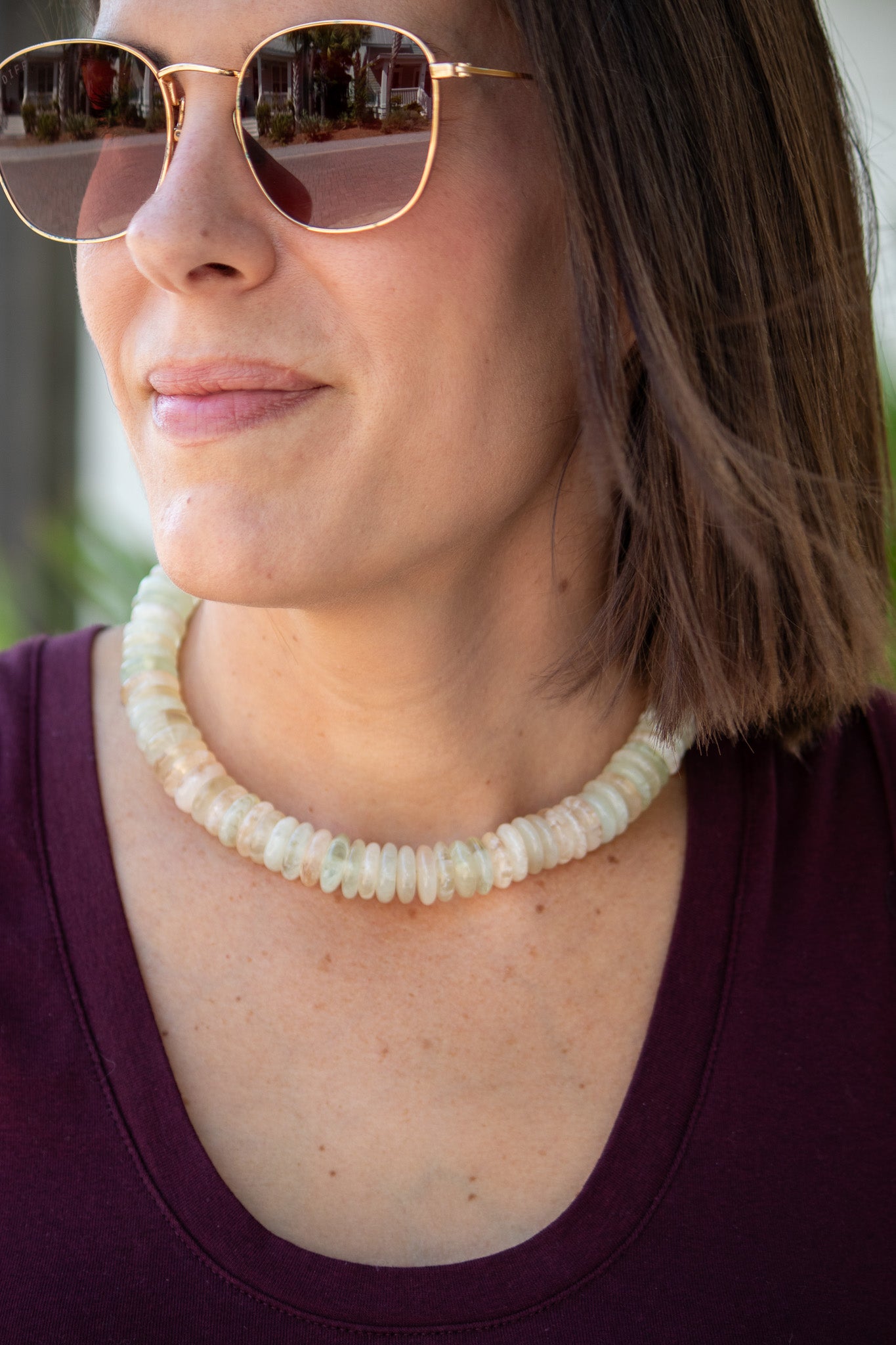 Woman wearing a beaded necklace and sunglasses with a blurred background