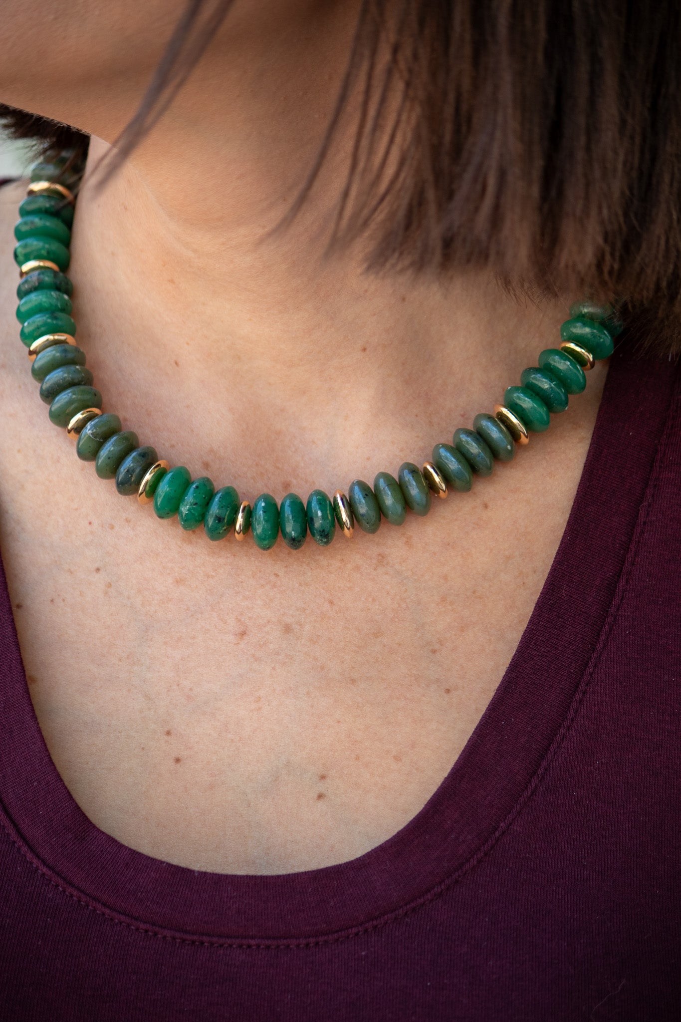 Green beaded necklace with gold accents on a person wearing a purple top.