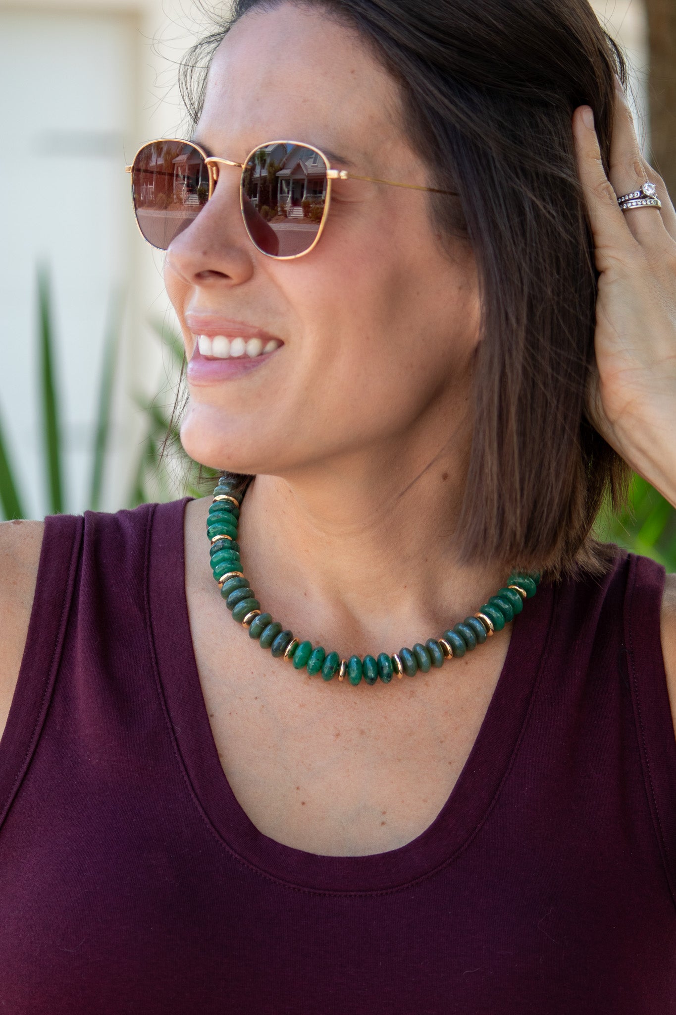 Woman wearing sunglasses and a green necklace, with blurred background
